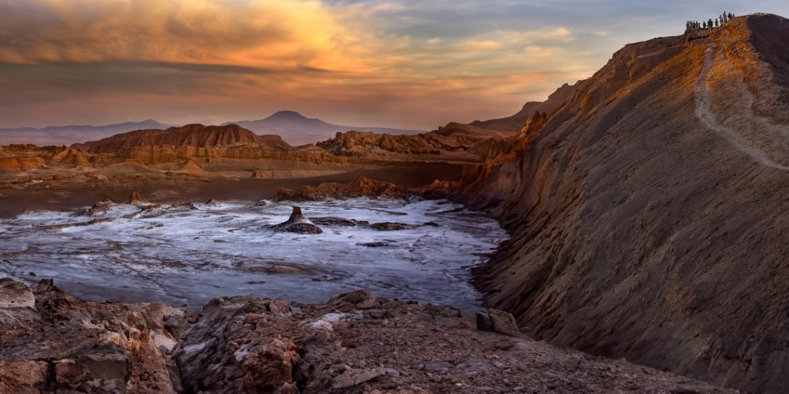 Tourists on a hilltop waiting for the sunset in the Valle de la Luna (Valley of the Moon) in the Atacama Desert, northern Chile, South America. The white areas on the valley floor are salt deposits.